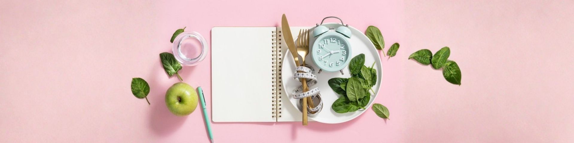 Carnet de notre avec une assiette sur laquelle i ly a des couvert, un mettre mesureur de taille, un réveil et des épinards, tout cela symbolise la minceur avec un verre d'eau et une pomme sur le côté, pour imagé le bandeau d'un article blog, 4 mythes fréquents sur la perte de poids.