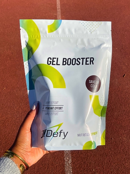 Sachet de Gel Booster, gel énergétique en poudre, saveur cola, tenu à la main sur une piste d'athlétisme, 1Defy Nutrition Sportive, made in bourgogne