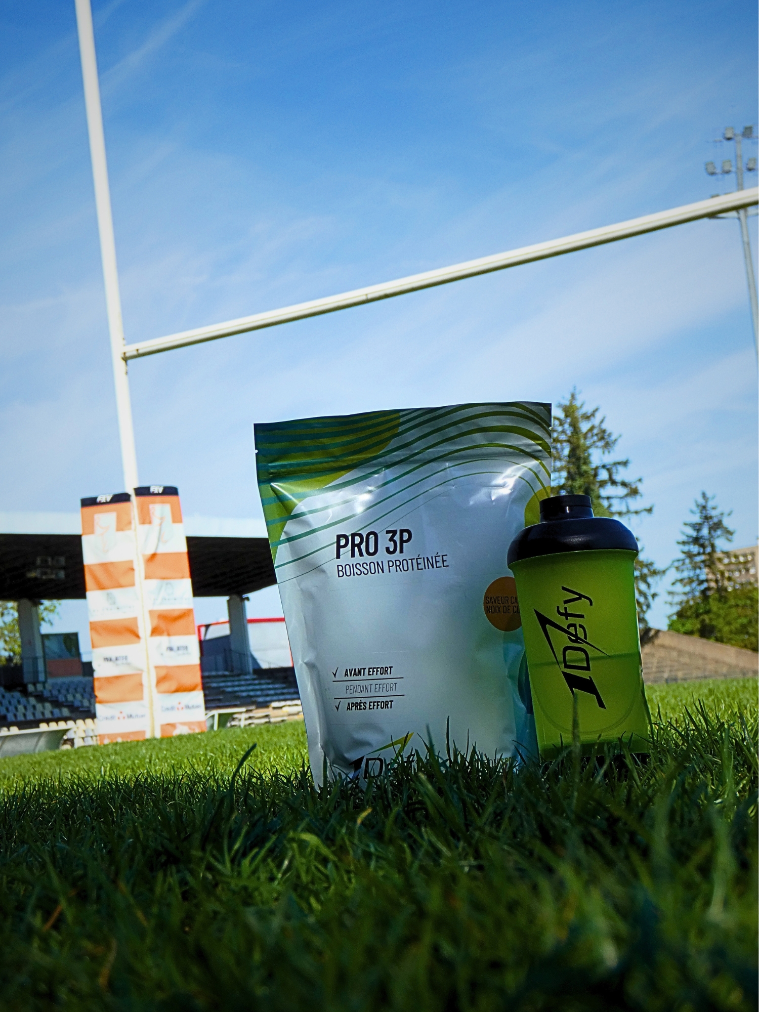 Sachet de Pro 3P saveur cacao coco avec un shaker devant des poteaux de rugby, 1Defy Nutrition Sportive Made in Bourgogne