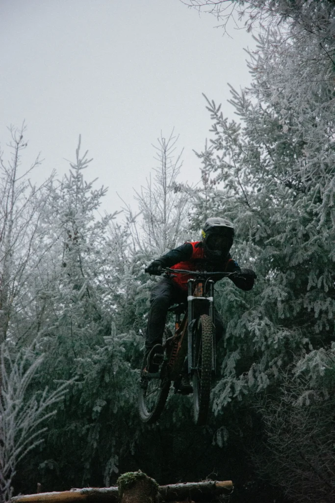 Matys Laureau, pilote 1Defy, réalisant un saut technique en VTT de descente (DH) dans un sous-bois forestier