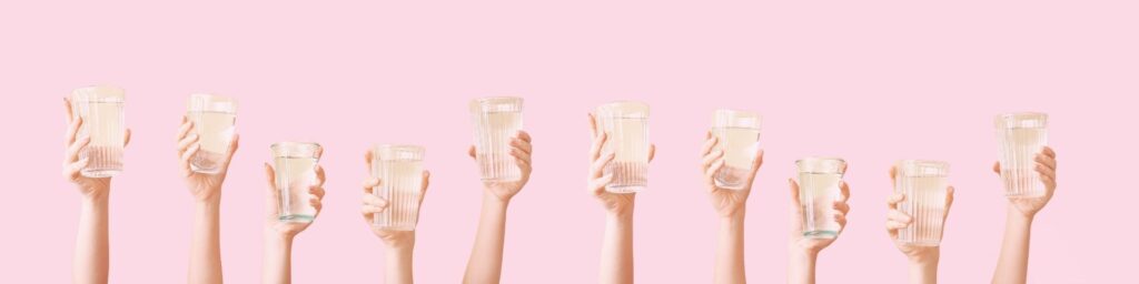 Image présentant plusieur mains tenant des verres d'eau pour illustrer l'article de blog 1Defy : Pourquoi boire de l'eau et en quelle quantité ?