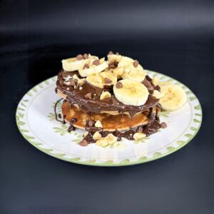 Pancakes protéinés avec une sauce en chocolat, des bananes coupées et des noisettes en topping, recette issues du blog de 1Defy nutrition sportive made in Bourgogne