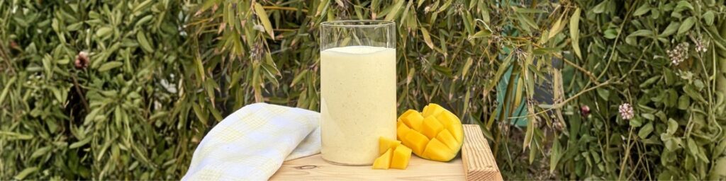 Lassi mangue coco protéiné dans un coin de verdure avec un morceau de mangue, recette issue du blog 1Defy nutrition sportive made in bourgogne