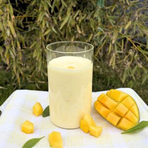 Lassi mangue coco protéiné dans un coin de verdure avec des morceaux de mangue, recette issue du blog 1Defy nutrition sportive made in bourgoggne