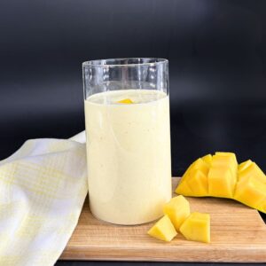 Lassi mangue coco protéiné sur une planche en bois avec des morceaux de mangue, recette issue du blog 1Defy nutrition sportive made in bourgogne