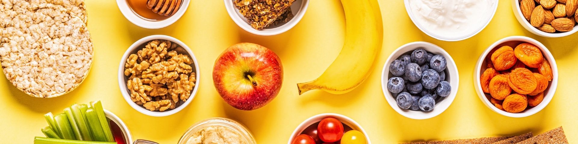 Image de couverture du blog : Faut-il manger avant le sport ? De 1Defy Nutrition Sportive Made in Bourgogne, photo avec une banane,une pomme, des oléagineux et d'autres aliments pouvant êter consommés avant le sport sur un fond jaune